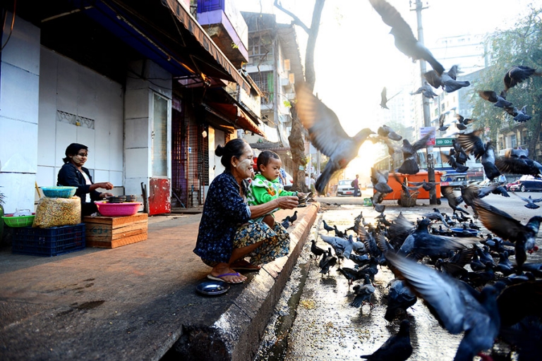 Woman feeding birds with grandson at dawn in downtown Yangon, Myanmar. - Kira Horvath Photography