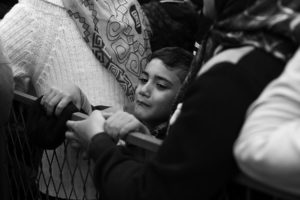 A syrian refugee boy cries as he is pushed in a crowd waiting for warm coats and blankets being handed out by the Red Cross. Refugee Crisis. - Kira Horvath Photography