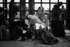 An Iraqi refugee plays with her daughter while waiting for a bus to the Hungarian boarder in Belgrade, Serbia. - Kira Horvath Photography